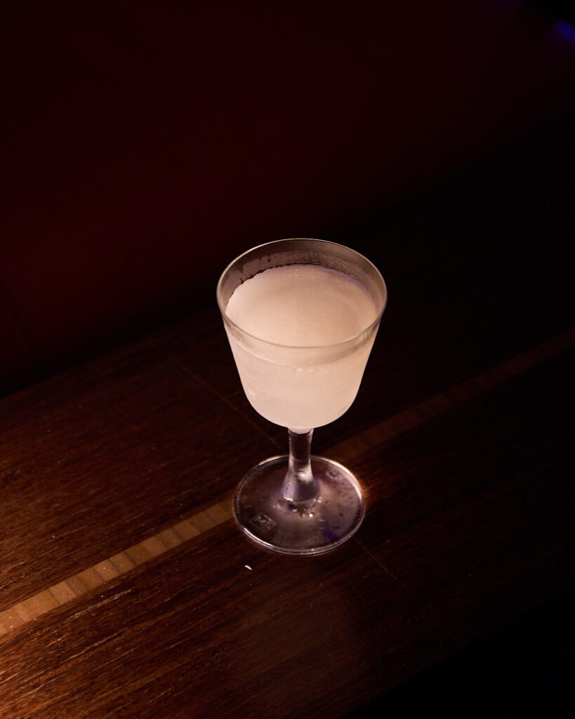 A frosty cocktail in a glass sits on a wooden table.