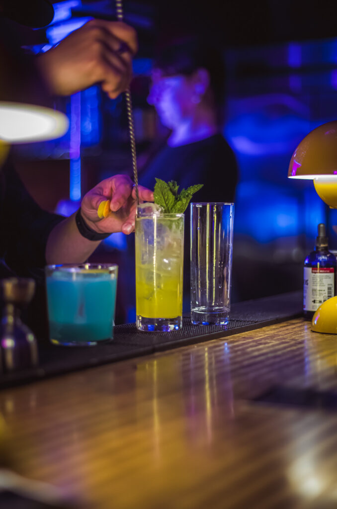 IMG_2413 Craft cocktail preparation at the "Play It Cool Pop-Up Bar Event," featuring vibrant blue and yellow drinks on a bar counter.