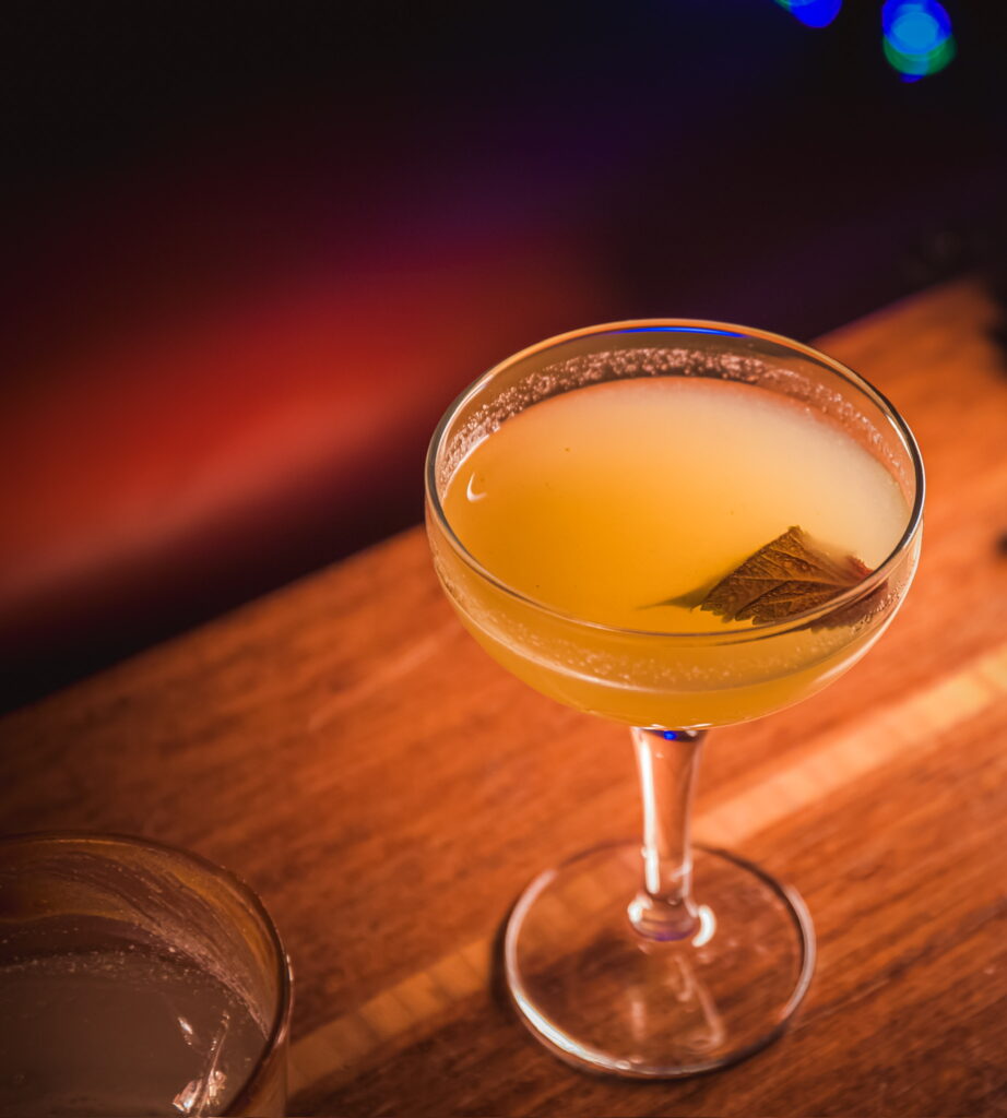 IMG_2436 A craft cocktail with a leaf garnish in a glass, featured at the "Play It Cool Pop-Up Bar Event."