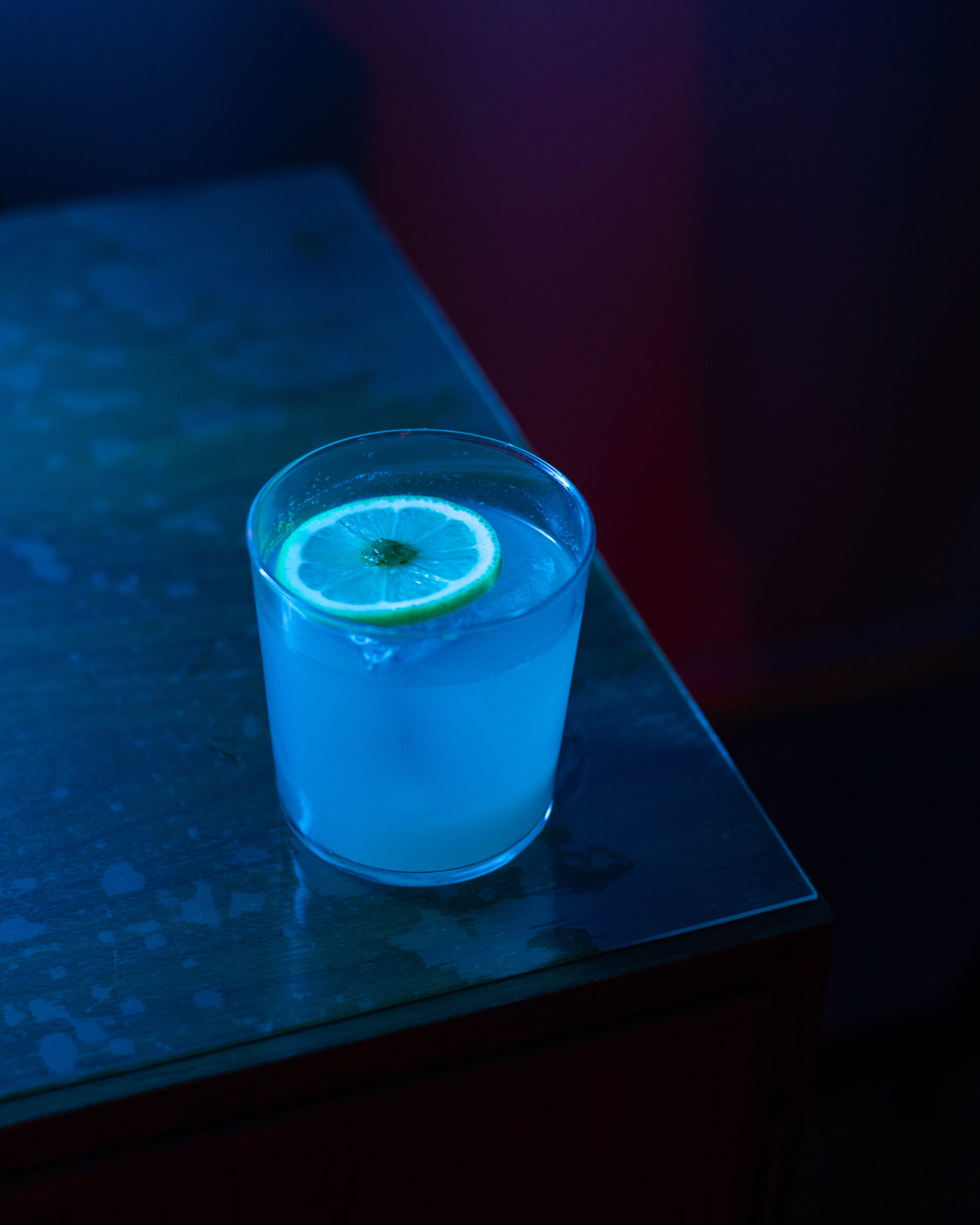 Glass of Lemon Drop Cocktail with a lemon slice, placed on a table under moody blue lighting.