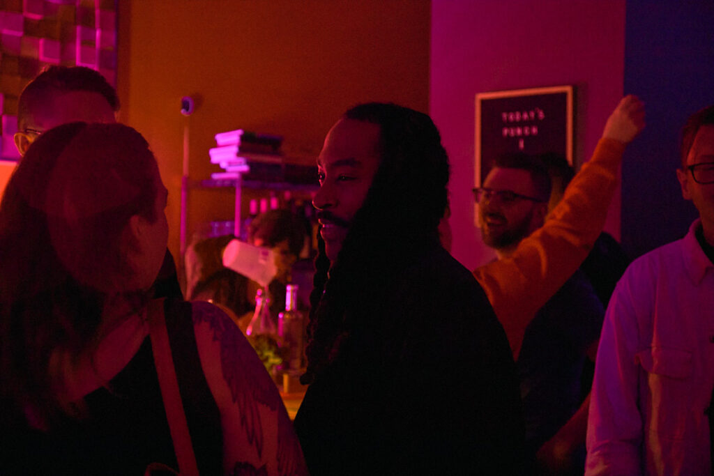A group of people socialize in a colorful, dimly lit space, engaging in conversation and laughter.